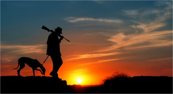 Man with Hunting Rifle walking with his Dog at Sunset